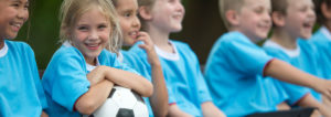 Young children sitting on the sideline of a soccer field