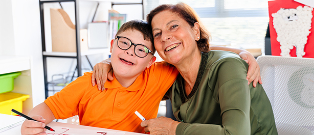 A boy with down syndrome is looking at camera in a classroom with his teacher