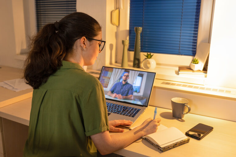 Rear view of young woman working at laptop. Remote work from home and online calling. Remote consultation with psychologist. Concept of modern freelancing and education.