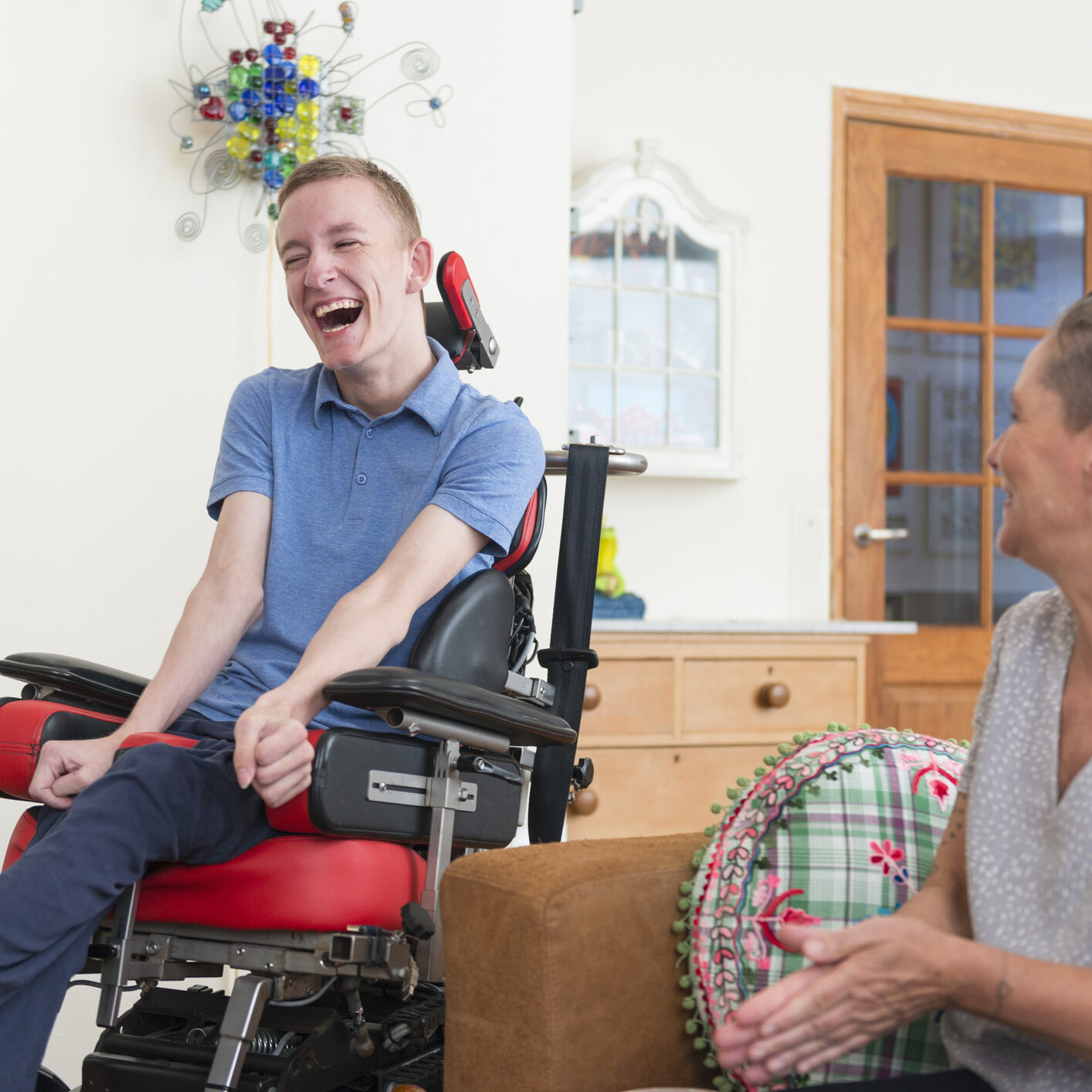 Color image of a real life young physically impaired ALS patient spending time with his mother at home. He is happy.